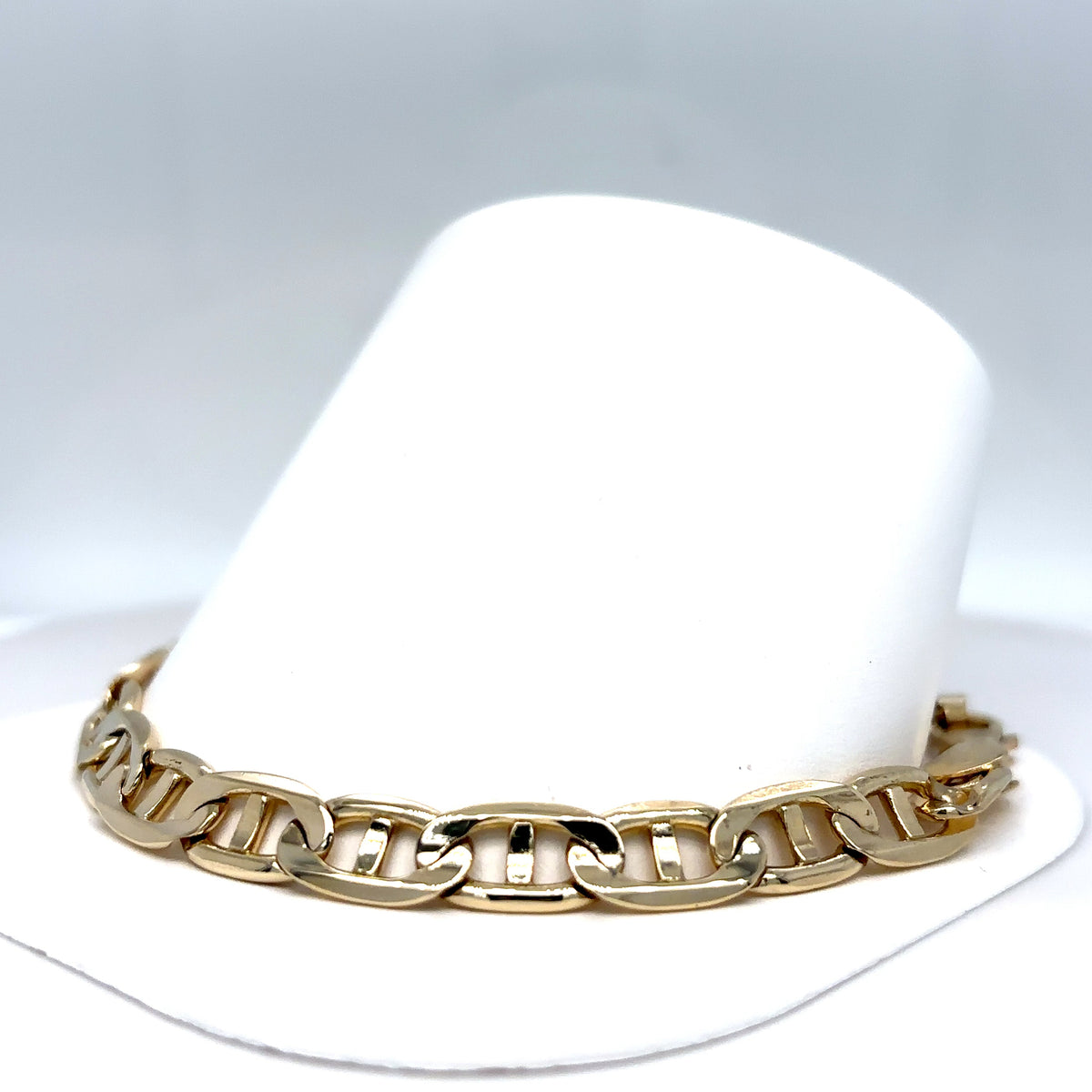 Gold chain bracelet on a white hat with a gray background