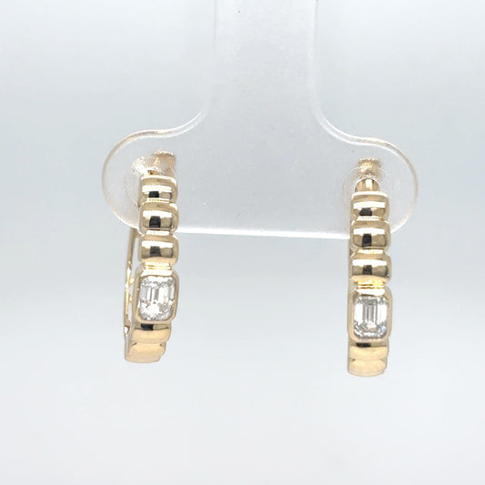 A pair of 14K yellow gold hoop earrings with emerald-cut diamonds, displayed on a clear stand against a light gray background.