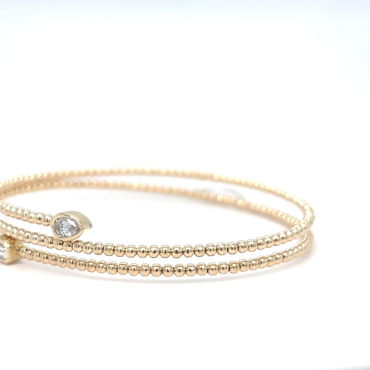 A 14K yellow gold beaded flex bangle bracelet with a pear-shaped diamond accent, photographed on a white background.