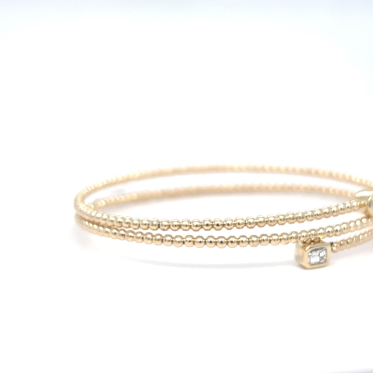 A delicate 14K yellow gold beaded flex bangle bracelet with a bezel-set emerald-cut diamond, photographed on a white background.