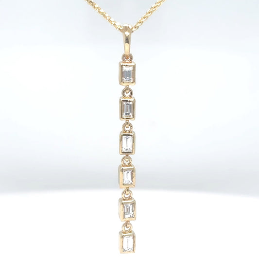 Close-up of a 14K yellow gold pendant with bezel-set baguette diamonds in a vertical line, suspended from a fine gold chain.
