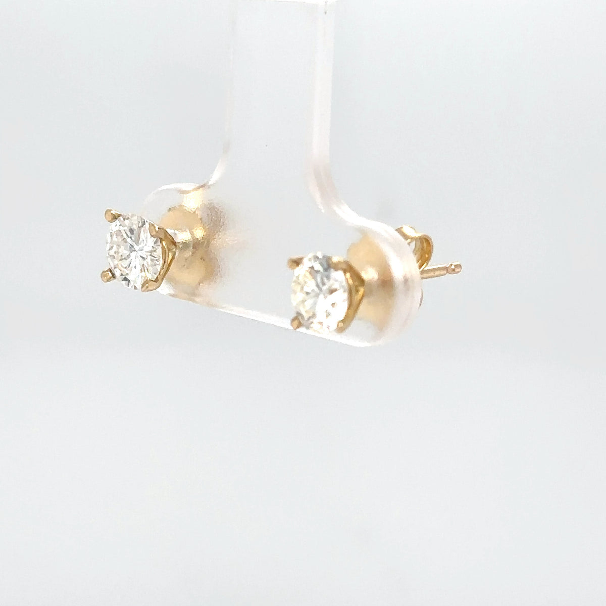 Gold stud earrings with clear gemstones on a light gray background