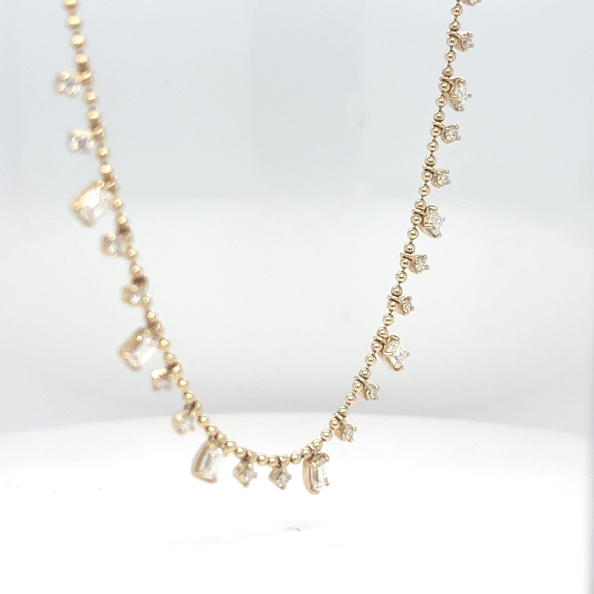 A 14K yellow gold bead chain necklace with dangling emerald-cut and round brilliant diamond drops, displayed against a white background.