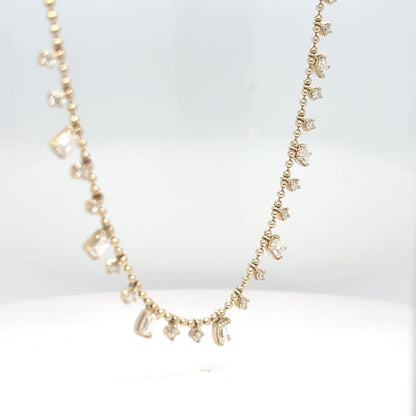 A 14K yellow gold bead chain necklace with dangling emerald-cut and round brilliant diamond drops, displayed against a white background.