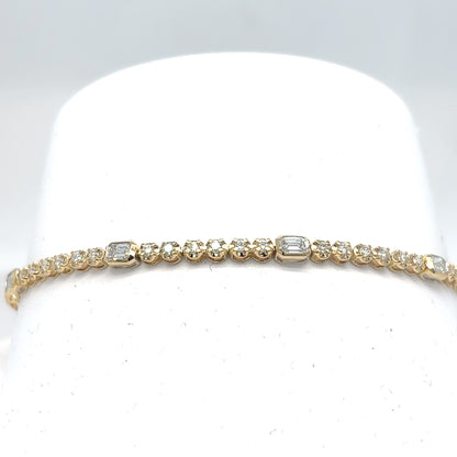 An 18K yellow gold tennis bracelet set with emerald-cut and round brilliant diamonds, displayed on a white cylindrical stand against a light gray background.